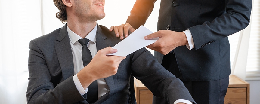 man in suit standing handing check to man in suit sitting at desk