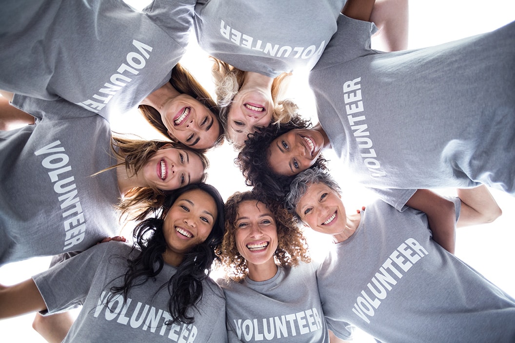 7 volunteers in grey t-shirts with volunteers on them in a circle with arms arounf each other looking down