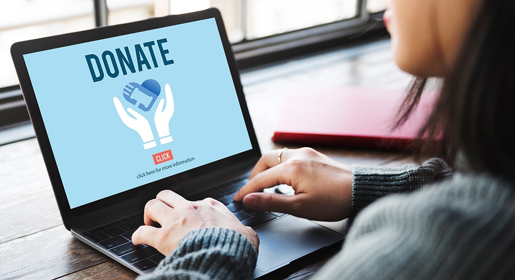 womans hand on laptop keyboard laptop screen reads DONATE with a CAT heart logo