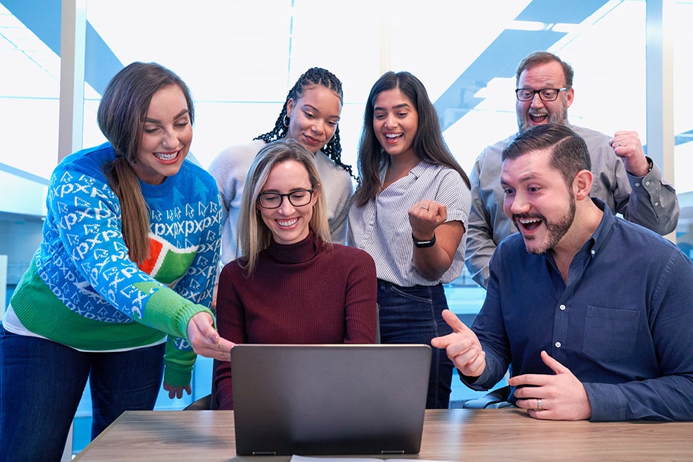 happy college students at table peering at a laptop and smiling