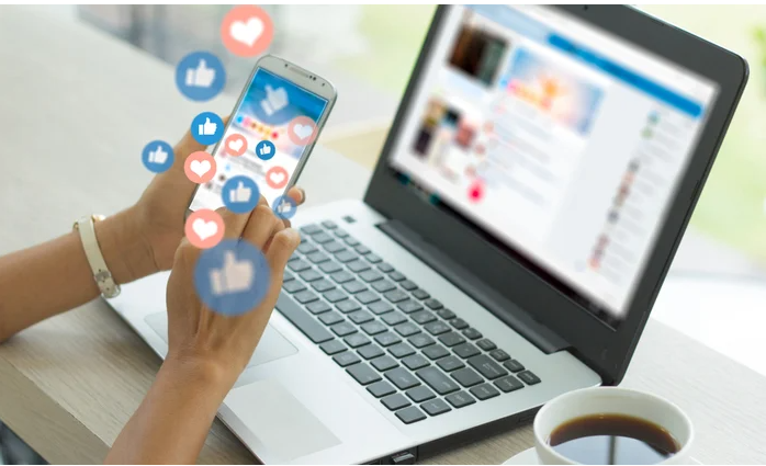 laptop on desk with woman hold mobile phone looking at social media