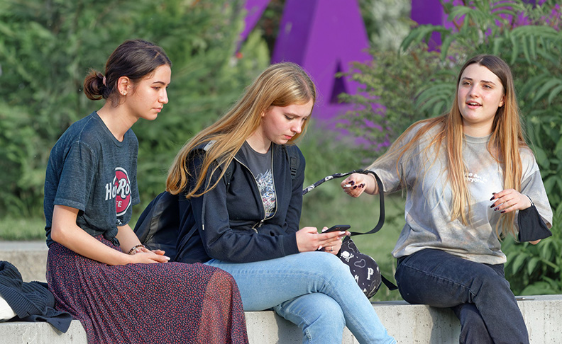 three young women sitting on a wall talking