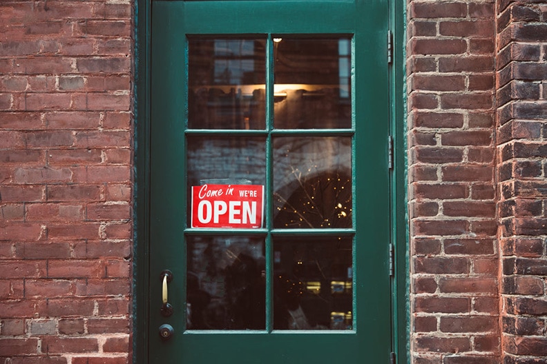 green door on brick building with sign reads were open