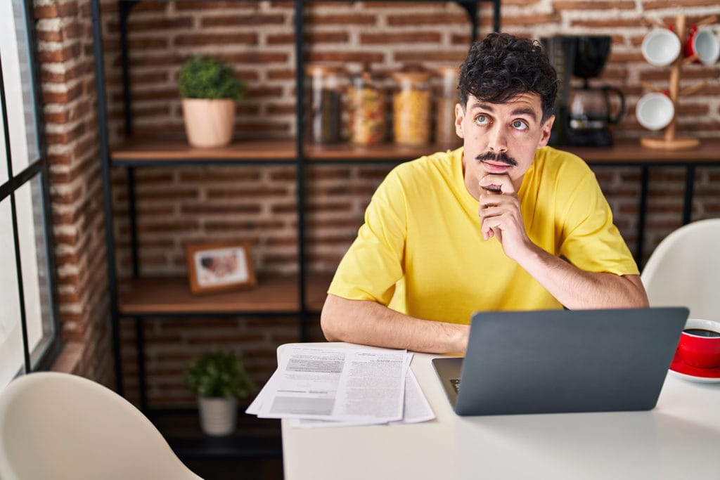 business owner sitting at desk with laptop hand on chin looking up at someone