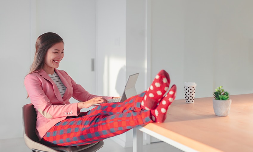 businesswoman in pink pajamas sitting at desk with feet up working on laptop
