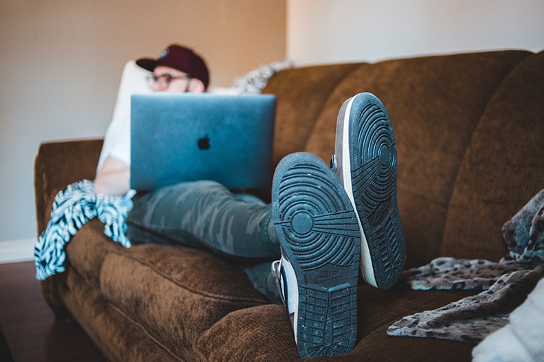 man lying on couch with laptop on lap watching tv and creating an online garage s ale