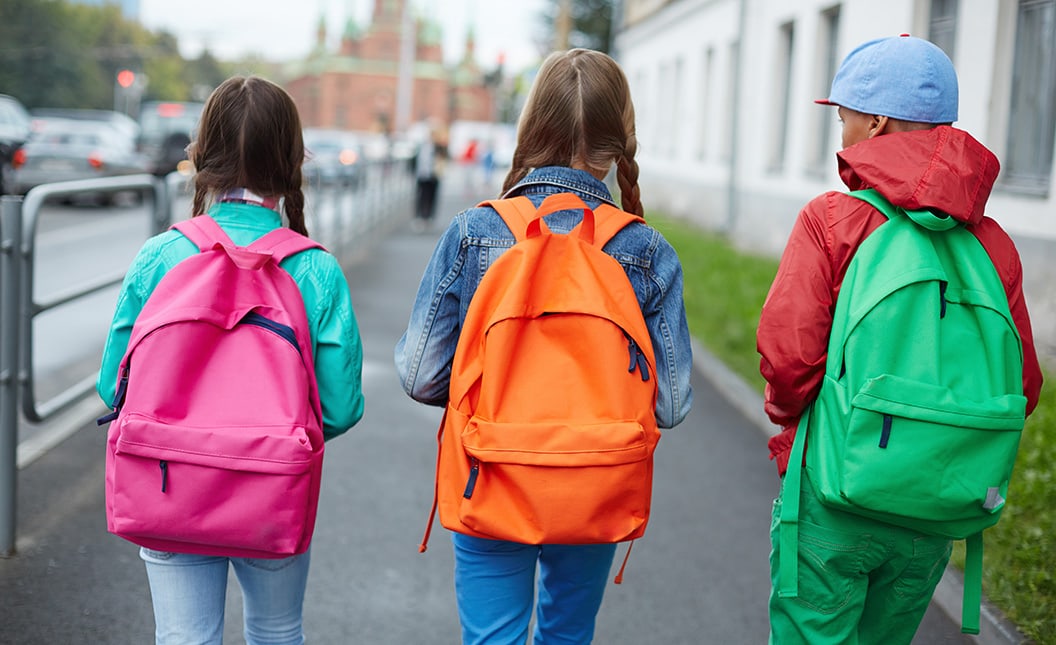 Backs of schoolkids with colorful backpacks moving in the street