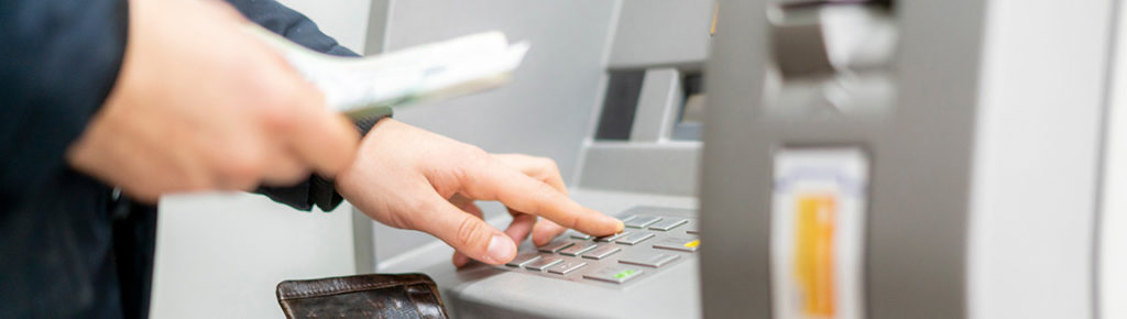 persons hand hold a wallet with cash and withdraw some money in ATM