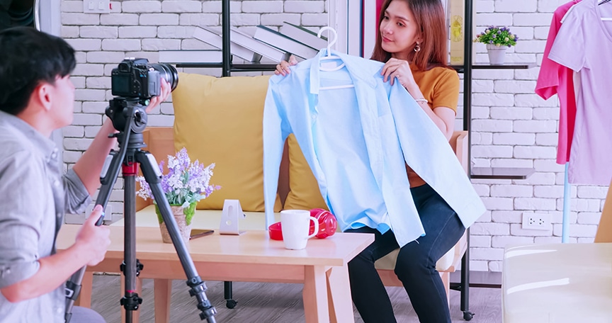 Young asian couple selling fashion clothes online by live streaming with digital camera.