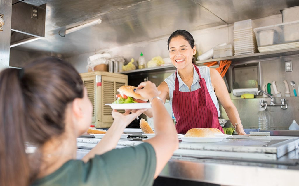 Happy woman selling hamburgers from a food truck handing one to a girl