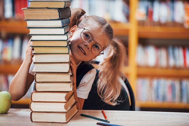 Cute little girl with pigtails is in the library. Apple on the books.