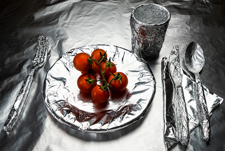 home plate, crockery and a glass covered with aluminum foil with some tomatoes