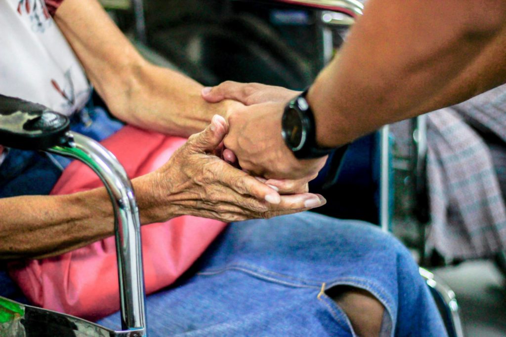 woman in wheelchair clasping hands with another person